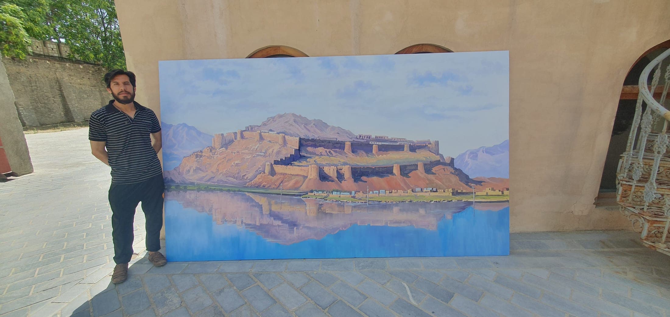 The artist standing beside a large panoramic canvas of a citadel reflected in water